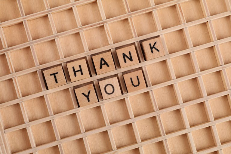 Wooden letter tiles spelling 'thank you' on a grid background, perfect for gratitude themes.