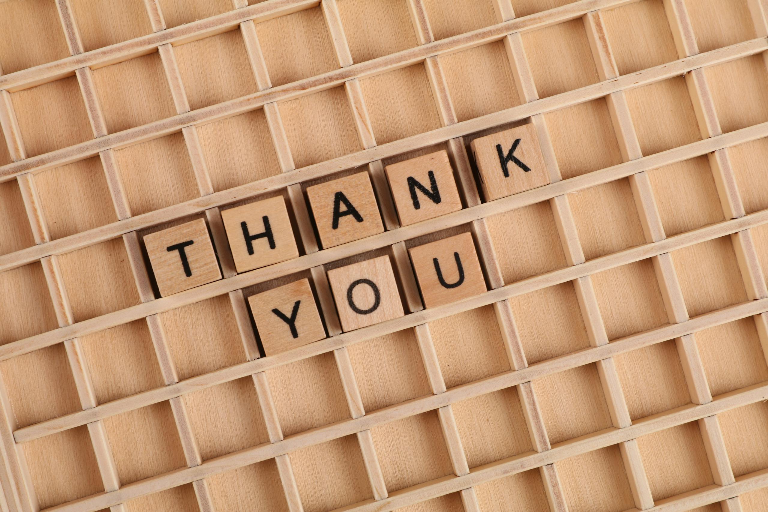 Wooden letter tiles spelling 'thank you' on a grid background, perfect for gratitude themes.