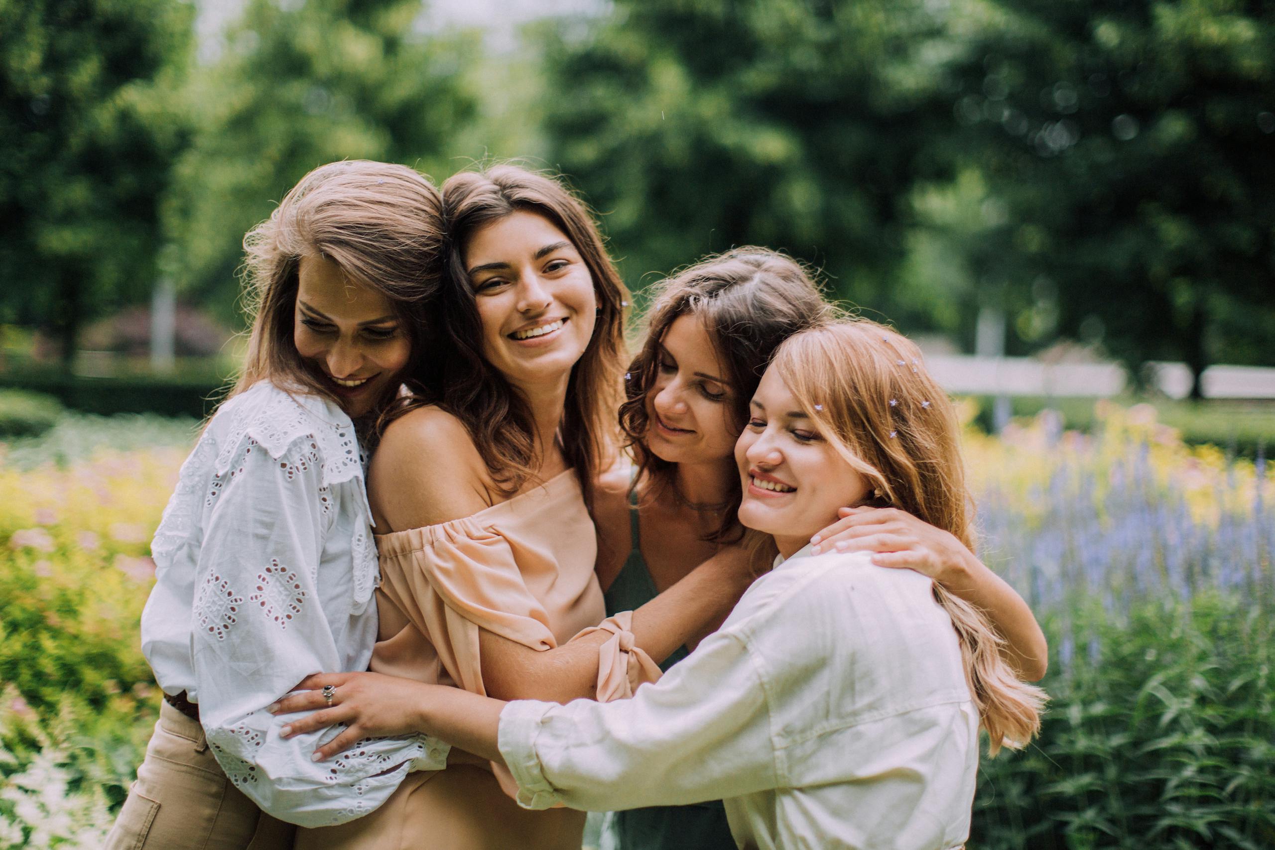 Four women joyfully embracing in a vibrant summer garden, celebrating friendship.